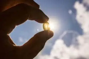 Hand holding a vitamin d supplement with the sun shining in the background