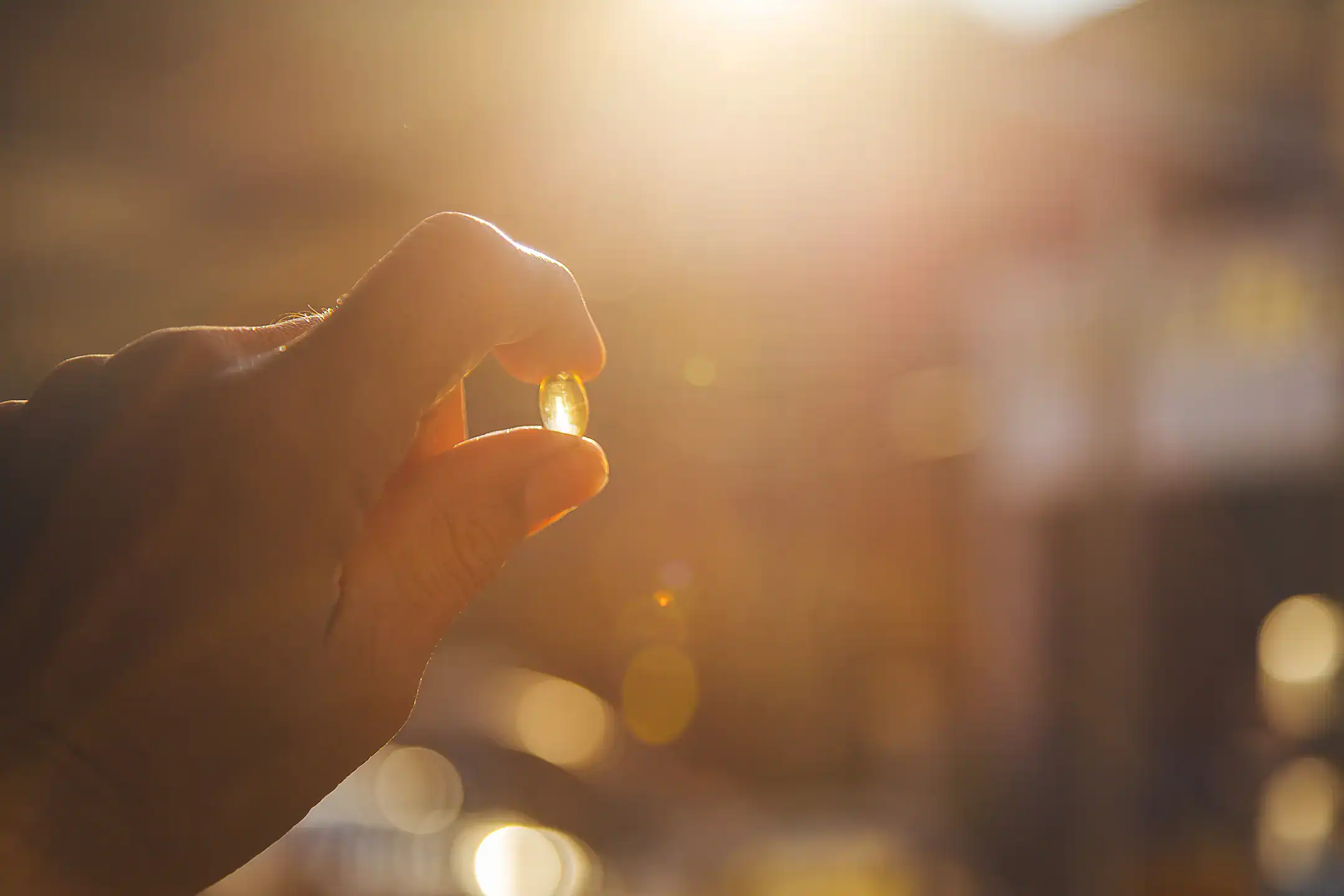 Hand holds a vitamin D tablet in front of the sun