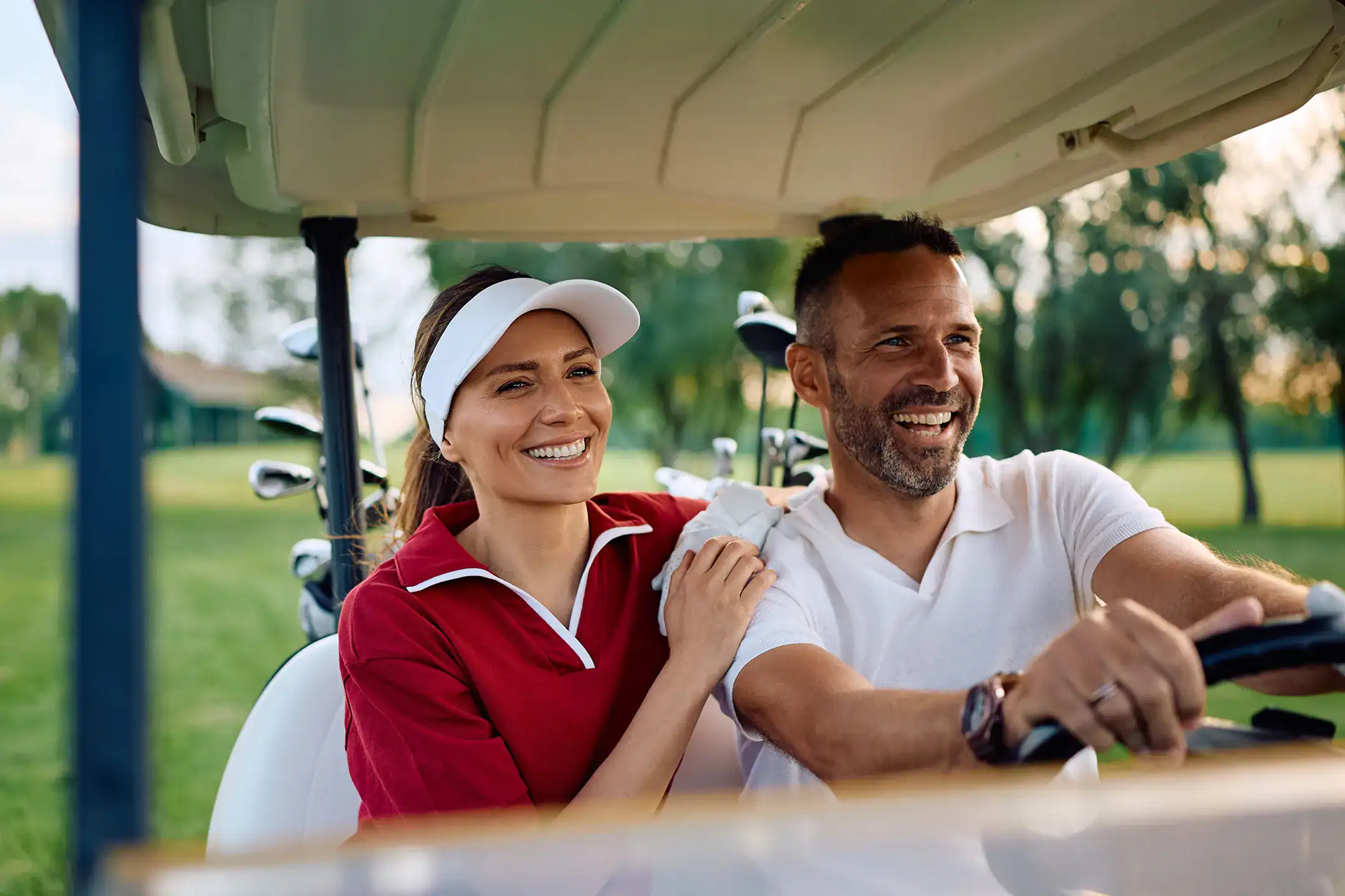 Smiling man drives golf cart with girlfriend next to him