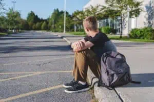 Teen boy with acne sitting alone on curb.
