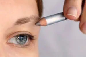 Woman applying eyebrow pencil to eyebrow to cover eyebrow thinning