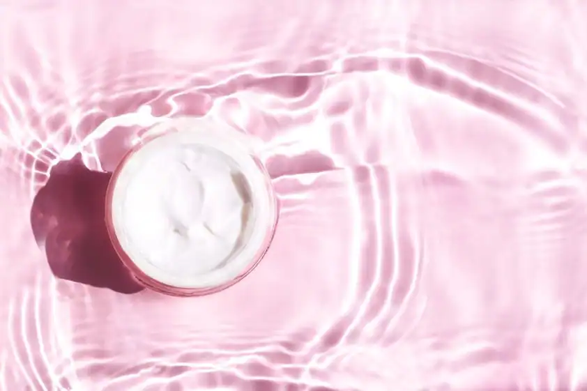 Moisturizer for dry skin on a pink surface with liquid around it
