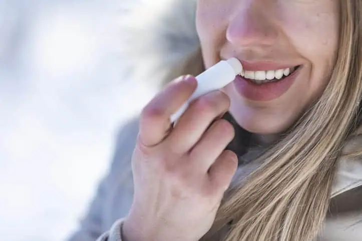 Woman applying lip balm to chappped lips.