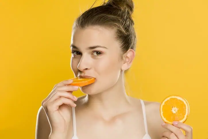 Woman eating oranges with an orange background behind her
