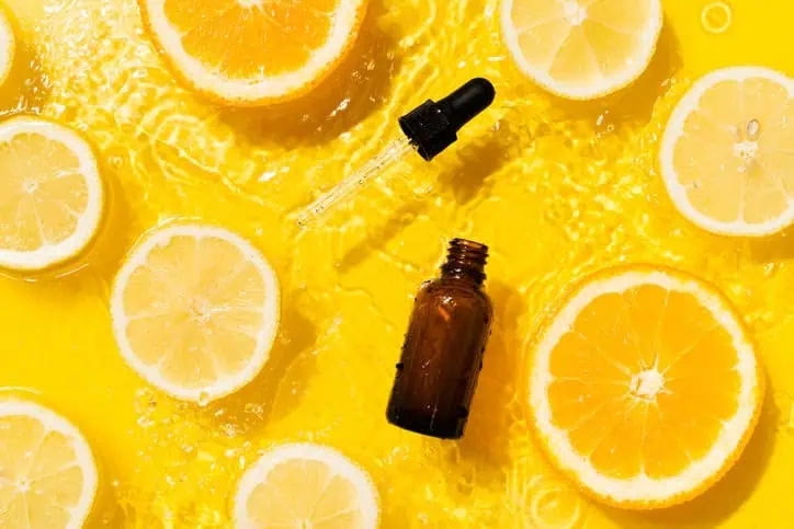 Eye dropper and bottle on a yellow background surrounded by citrus fruits.