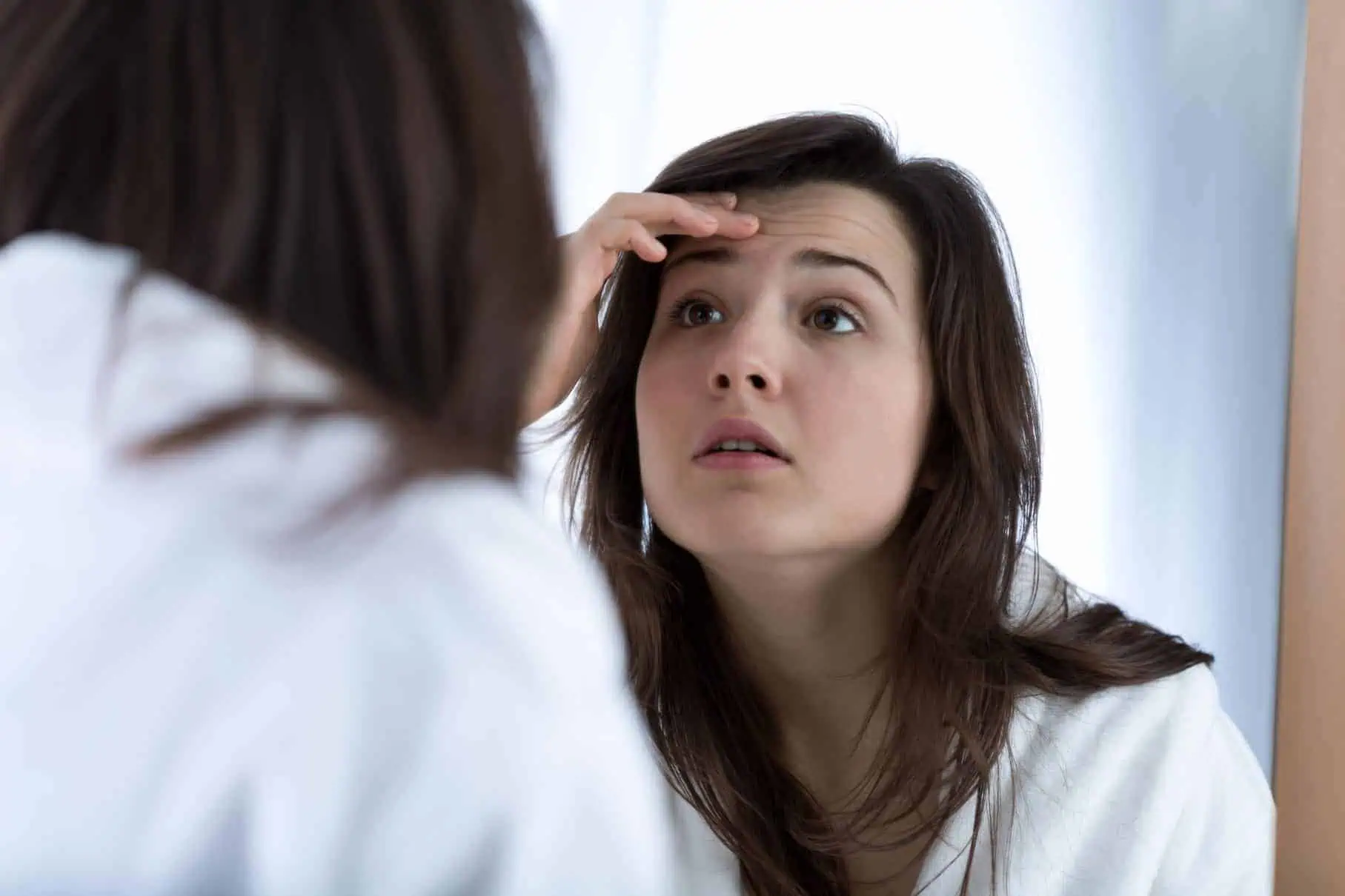 teenage girl examines her face in the mirror, worried about teen acne